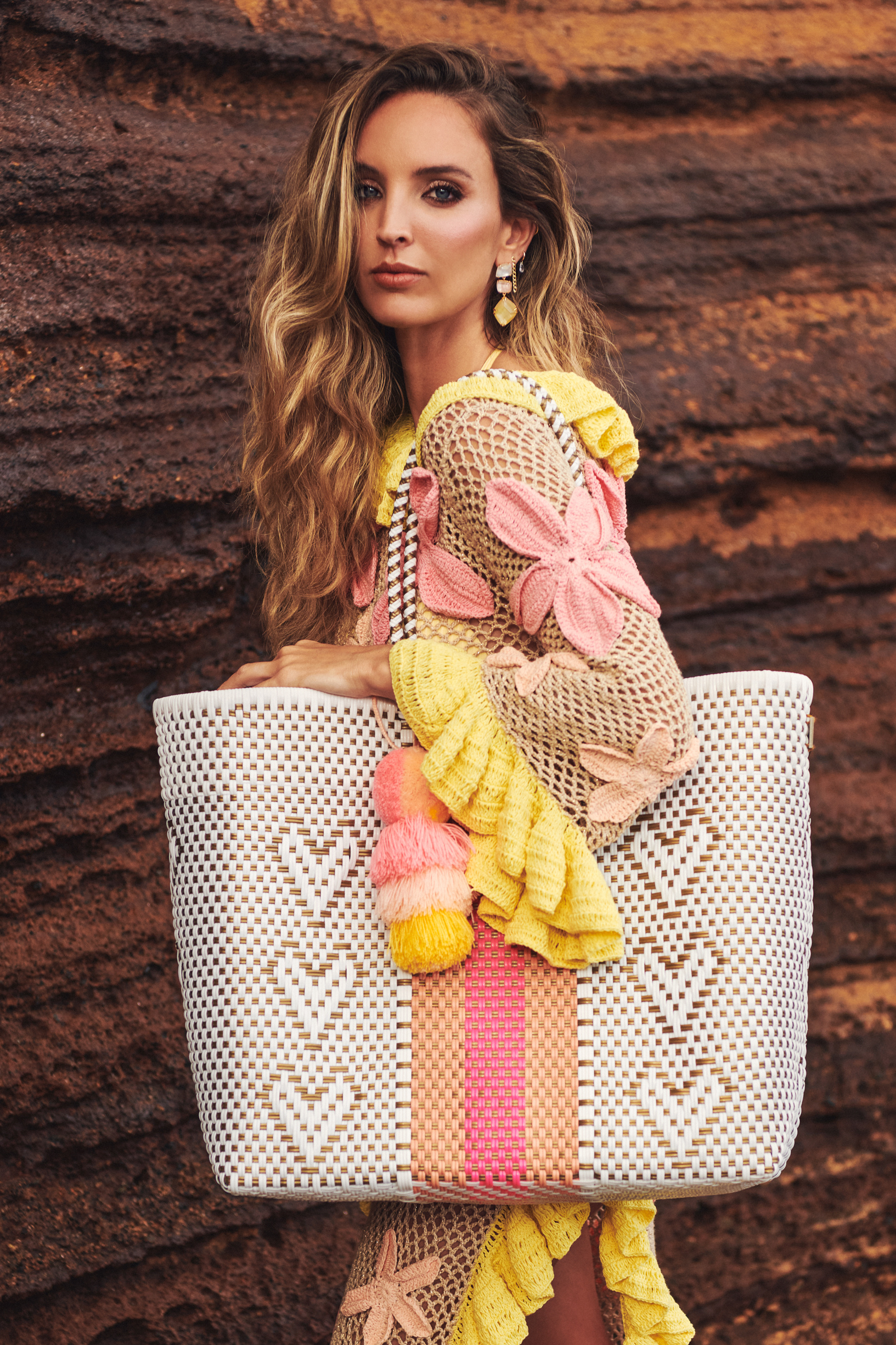 A woman holding a white and multicolored handcrafted tote bag made from recycled plastic, featuring pom-pom details.
